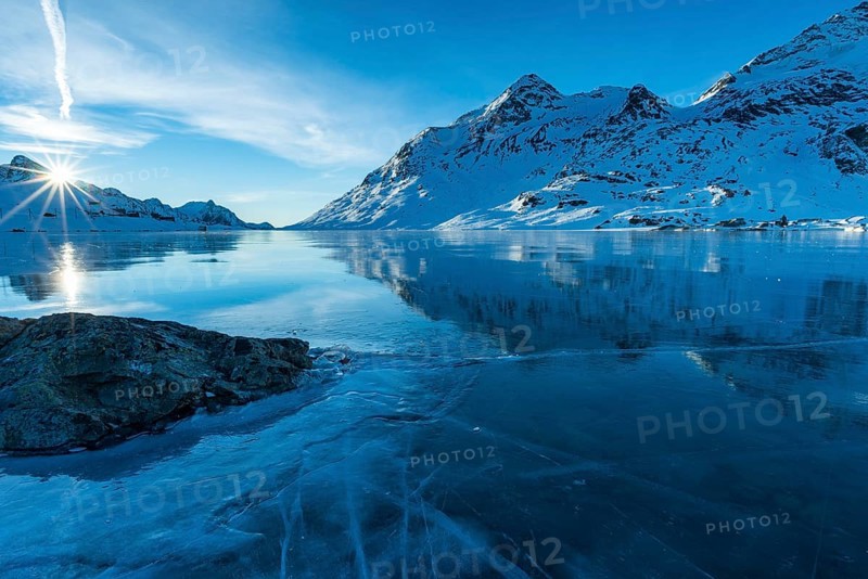 Ice structures and rock in the black ice of the frozen Lago Bianco in the Swiss mountains