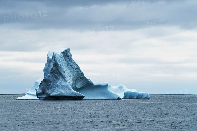 Iceberg drifting on the open sea against a dark cloudy sky