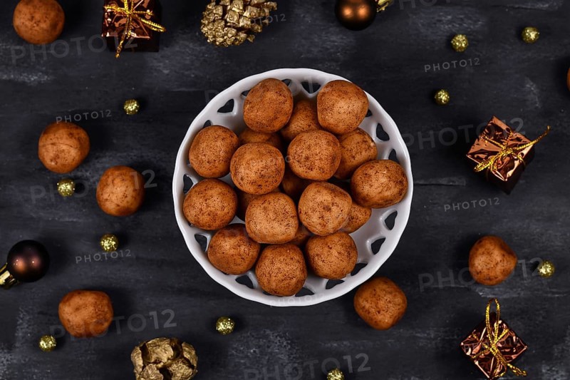 Traditional German Christmas sweets called Marzipankartoffeln. Round ball shaped almond paste pieces covered in cinnamon and cocoa powder in white bowl on dark background