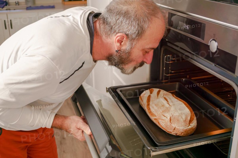 Older man with beard putting bread in the oven of his house