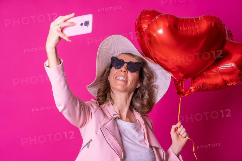 Blond caucasian woman having fun in a white hat and sunglasses in a nightclub with some heart balloons