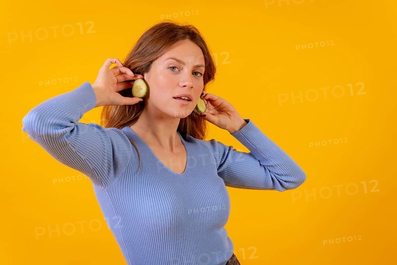 Vegan woman with earrings cucumber slices on a yellow background