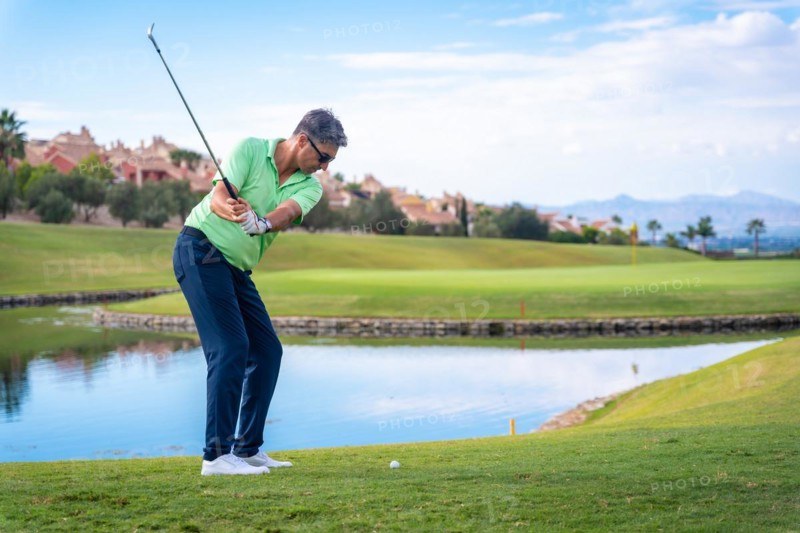 Man playing golf at golf club by a lake