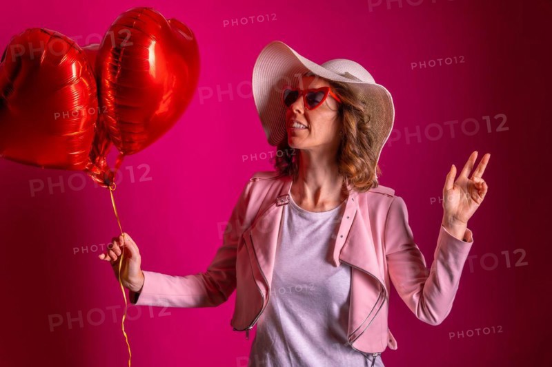 Portrait of a caucasian woman enjoying dancing with a white hat in a nightclub with some heart balloons