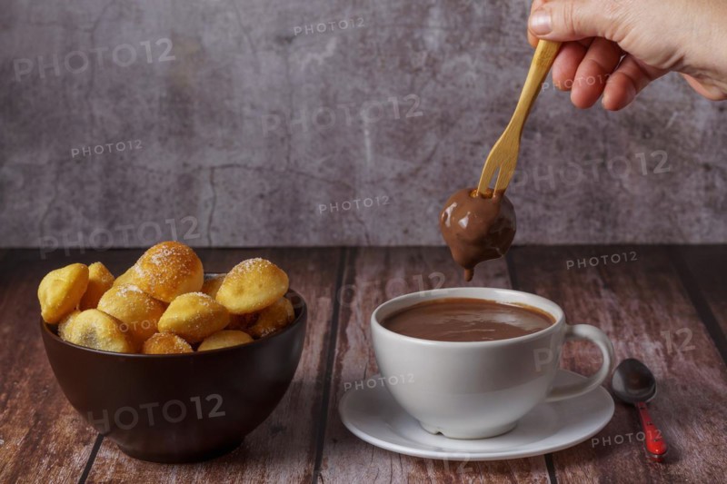 Woman spreading a sugared doughnut with a wooden fork on a hot chocolate in a white mug