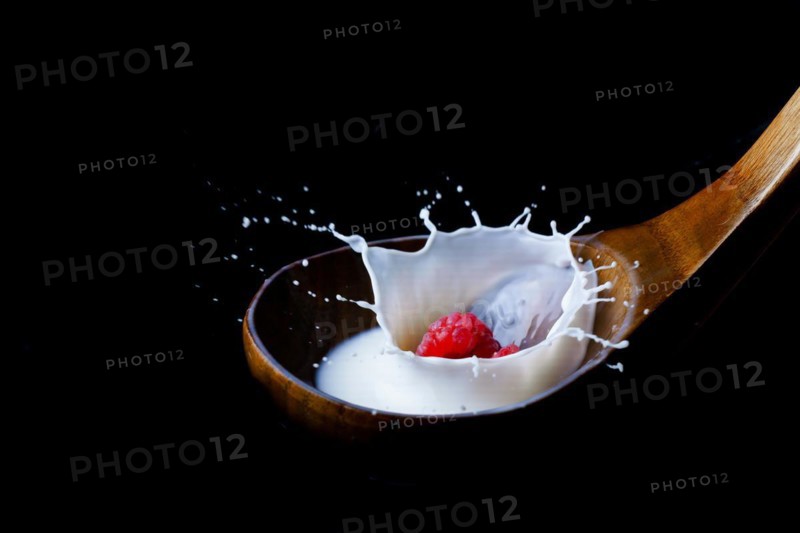 Fresh raspberry splashing milk on a wooden spoon