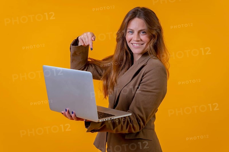 Business woman pointing at a computer on a yellow background