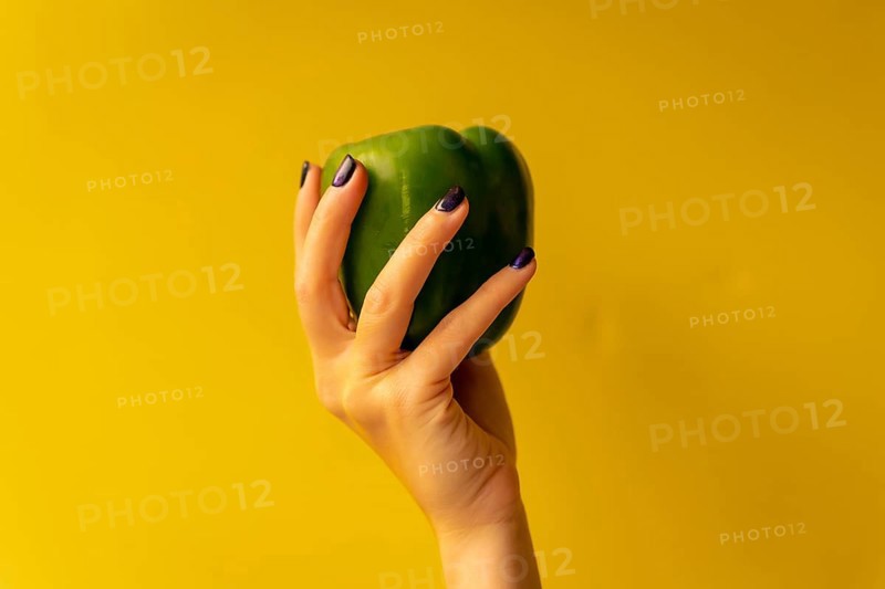 Woman's hand with a vegetable on a yellow background