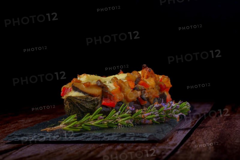 Eggplants stuffed with meat and vegetables with rosemary branch in flower and tomato cut on a black background