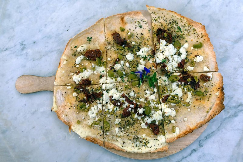 Flammkuchen with olives dried tomatoes and feta cheese on a wooden board