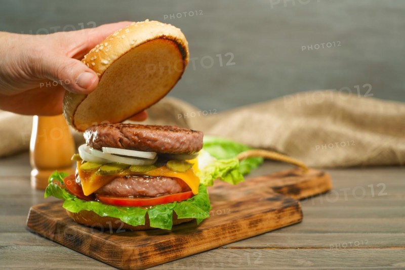 Close-up of a woman's hands opening the bun of a hamburger bun complete with two pieces of meat on a wooden board