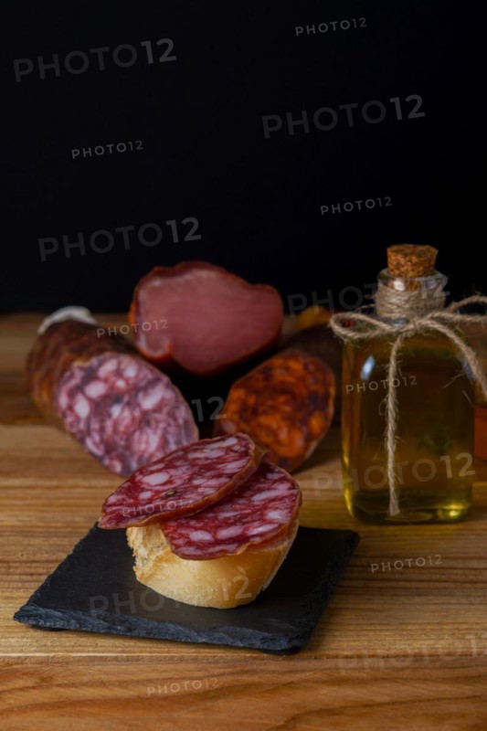 Tapa of iberian sausage on rustic bread with olive oil on a wooden board with black background
