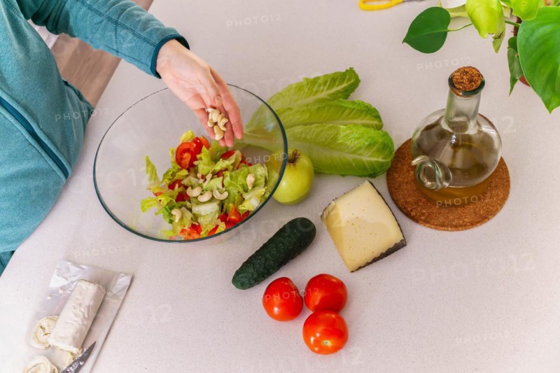 Woman adding cashews to a healthy salad at her kitchen table