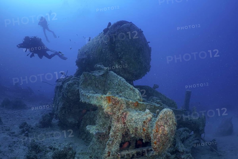 Remains of a steam locomotive from the Second World War on the seabed. Divers in the background. Dive site Thistlegorm wreck