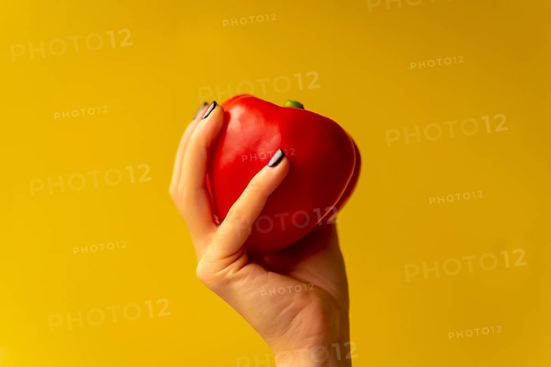 Woman's hand with a vegetable on a yellow background