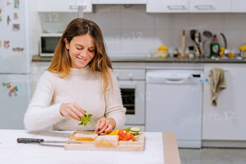 Vegetarian woman cooking a vegetable sandwich in the kitchen at home. Placing the arugula