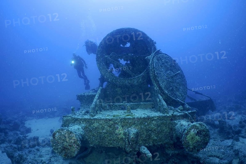 Remains of a steam locomotive from the Second World War on the seabed. Divers in the background. Dive site Thistlegorm wreck