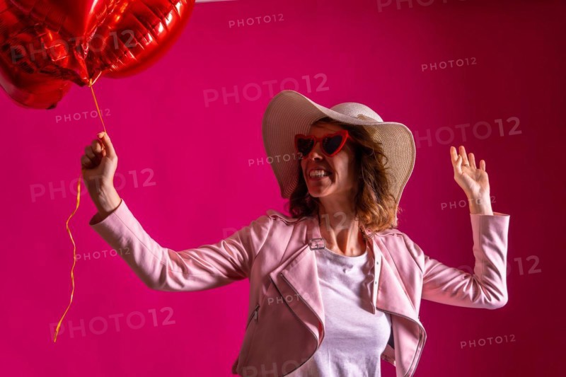 A caucasian woman enjoying dancing with a white hat in a nightclub with some heart balloons