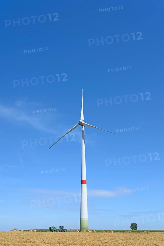 Wind turbine at a stubble field with round bales of straw
