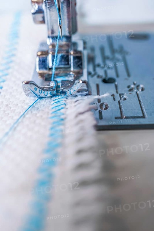 Close-up of sewing machine needle with blue thread sewing on a white fabric