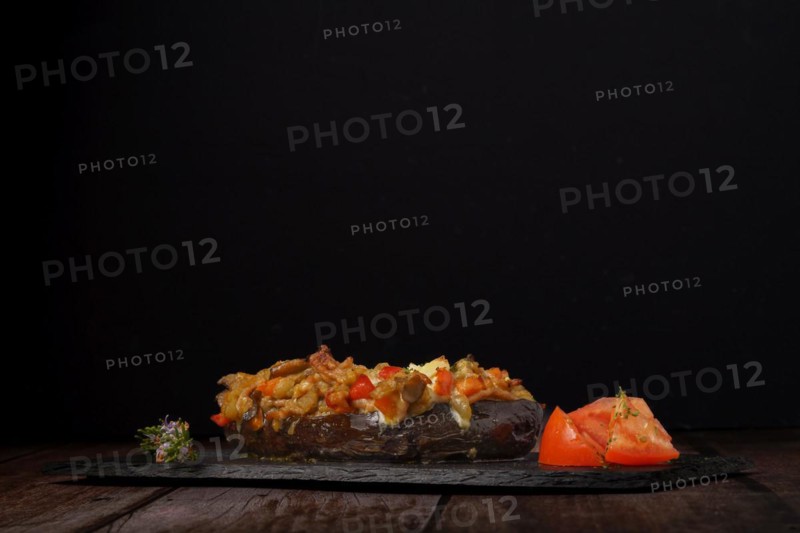 Eggplants stuffed with meat and vegetables with rosemary branch in flower and tomato cut on a black background