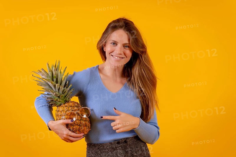 Woman with a pineapple in sunglasses in a studio on a yellow background