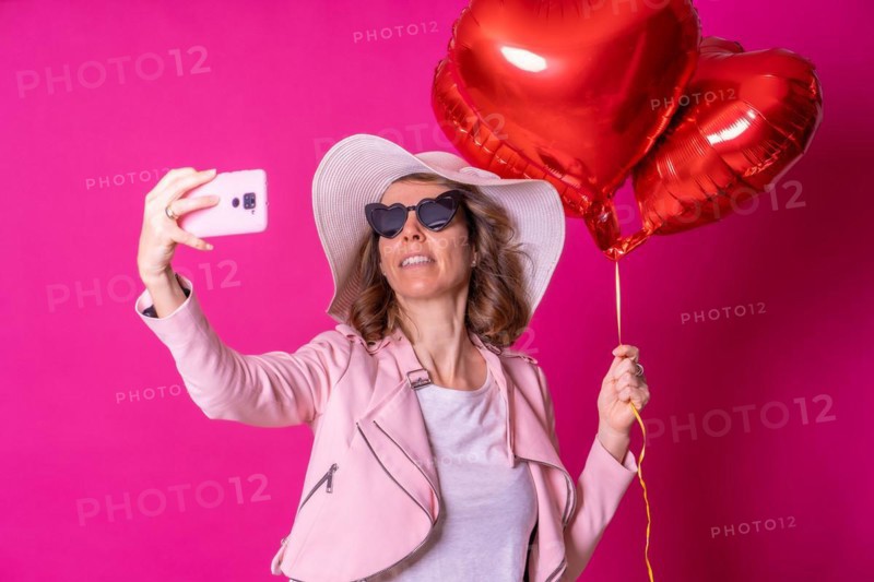 A blonde caucasian woman having fun with a white hat and sunglasses in a nightclub with some heart balloons