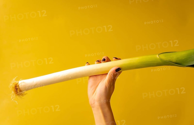 Woman's hand with a vegetable on a yellow background