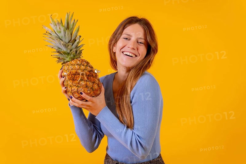 Girl smiling with a pineapple in sunglasses in a studio on a yellow background