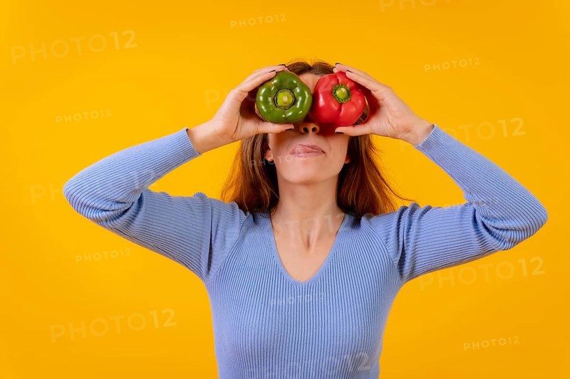 Vegetarian woman in a portrait with peppers in her eyes on a yellow background