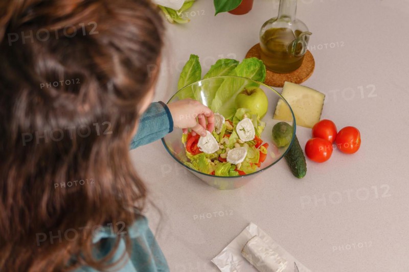 Above view of a woman adding goat cheese to a healthy salad at her kitchen table