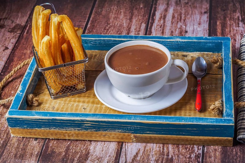 Hot chocolate in a white mug with churros in a blue wooden tray on a wooden table