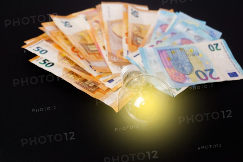 Lighted light bulb with euro banknotes in the background on a black background