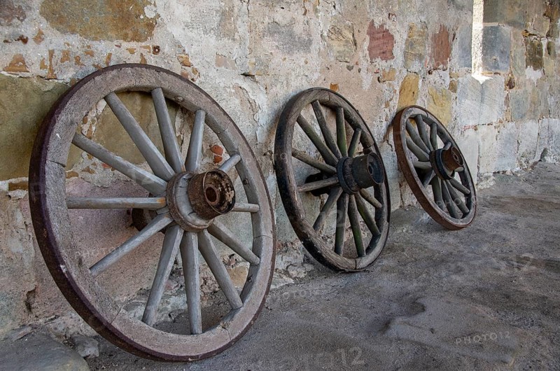 Historic old carriage wheels of carriages stand against an old sandstone wall