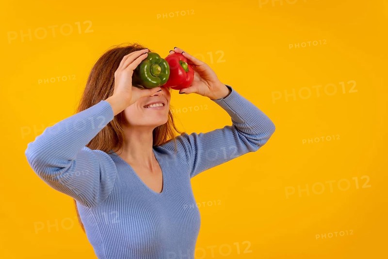 Vegetarian woman with spyglasses of peppers on her eyes on a yellow background