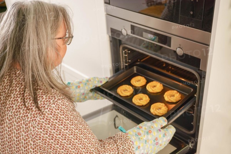 Older white-haired woman putting a tray of cookies in the oven