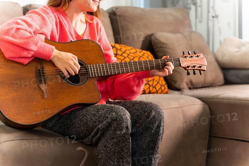 Playing the guitar at home sitting on the sofa in her living room next to the sale