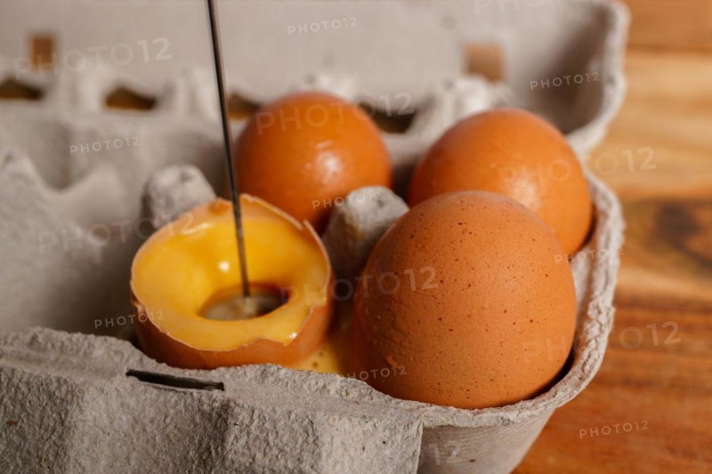 Woman beating an egg in its own shell with a small blender