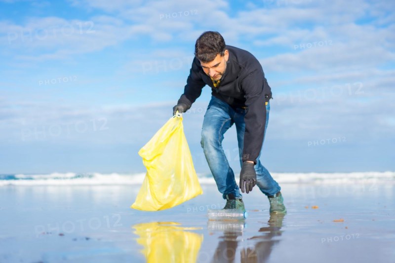 Volunteer man collecting garbage or plastic on the beach. Ecology concept