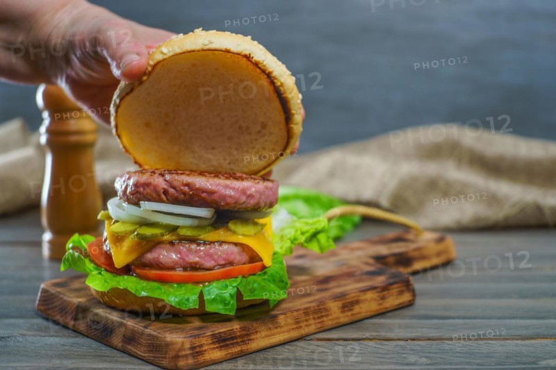 Close-up of a woman's hands opening the bun of a hamburger bun complete with two pieces of meat on a wooden board