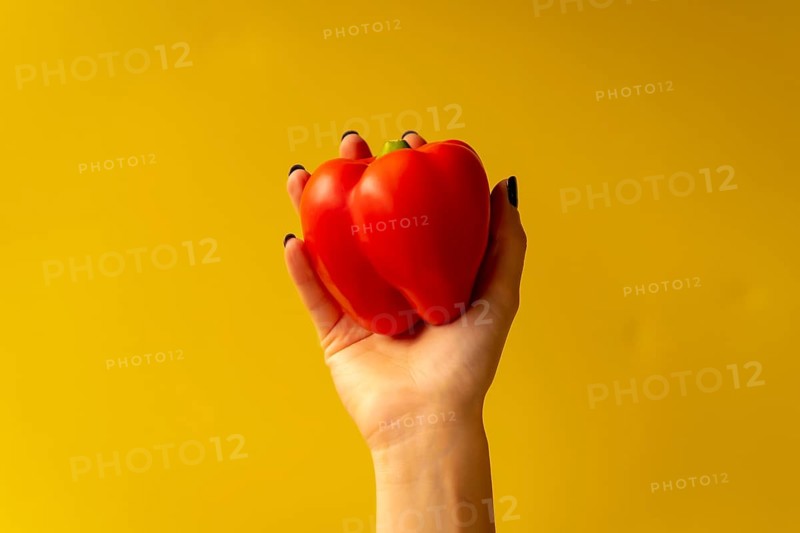 Woman's hand with a vegetable on a yellow background
