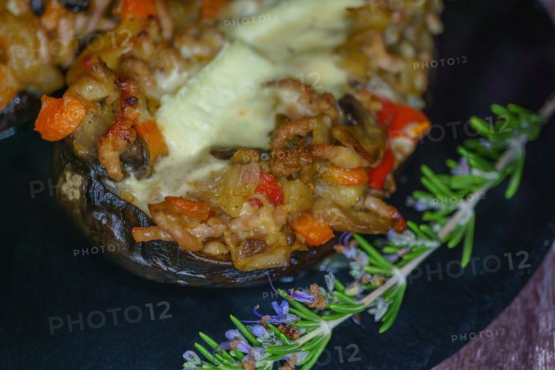Foreground eggplant stuffed with meat and vegetables covered with bechamel sauce on a black slate on a wooden table