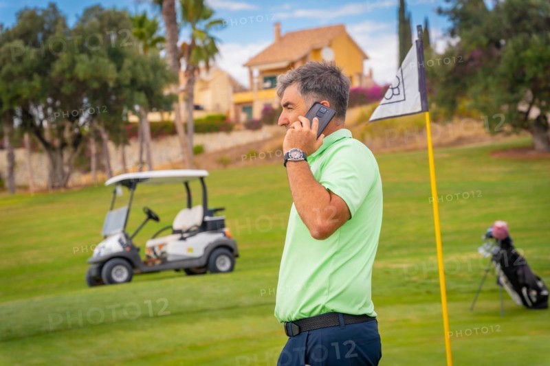 Businessman playing golf and answering a work call with the phone from the club