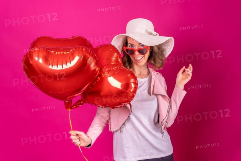Portrait of a caucasian woman having fun dancing with a white hat in a nightclub with some heart balloons