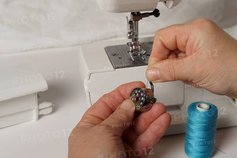 Close-up of a woman's hands putting blue thread on a sewing machine