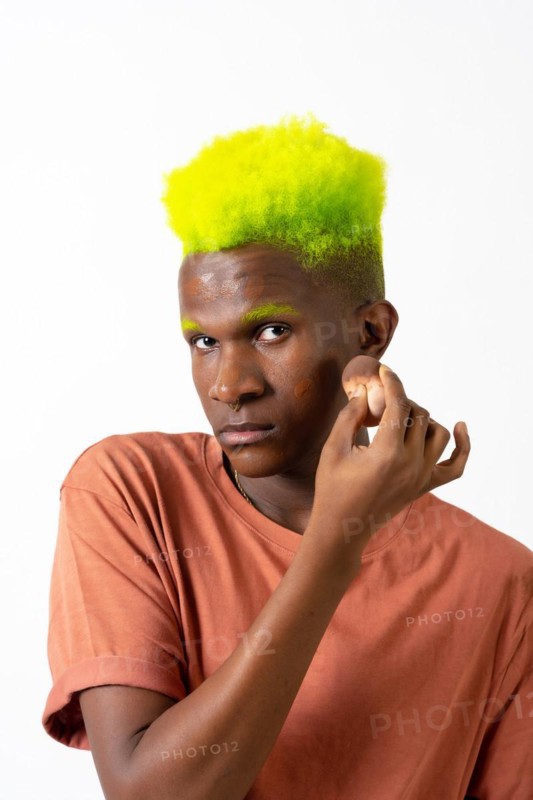 An androgynous black man posing putting on makeup