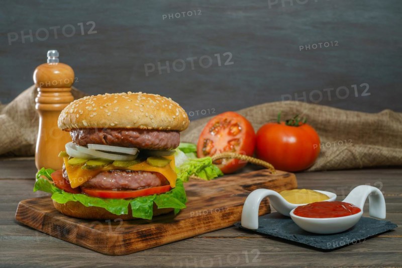 Close-up of a delicious whole hamburger on a wooden board and sauces