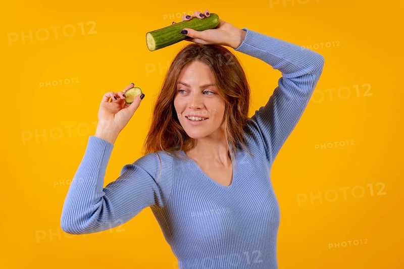 Portrait of a vegan woman holding a cut cucumber on a yellow background