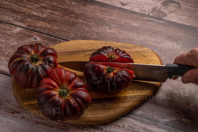 Close-up of a woman's hand with knife cutting tomatoes on a board on wooden table