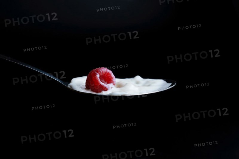 Raspberry splashing milk on a metal spoon splash effect with black background